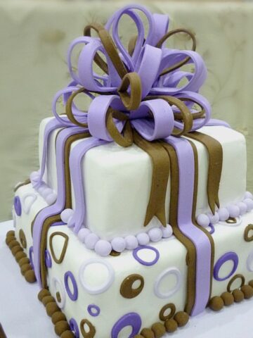 A 2 tier square cake decorated with fondant loop bow in violet and brown.
