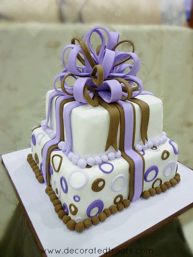 A 2 tier square cake decorated with fondant loop bow in violet and brown