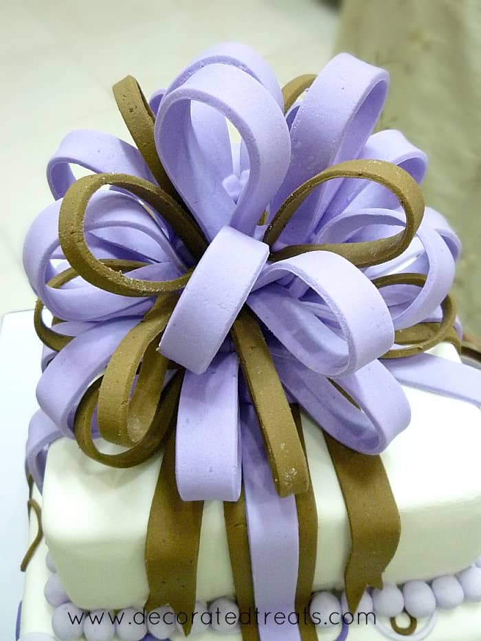 A violet and brown fondant loop bow on top of a 2 tier square cake