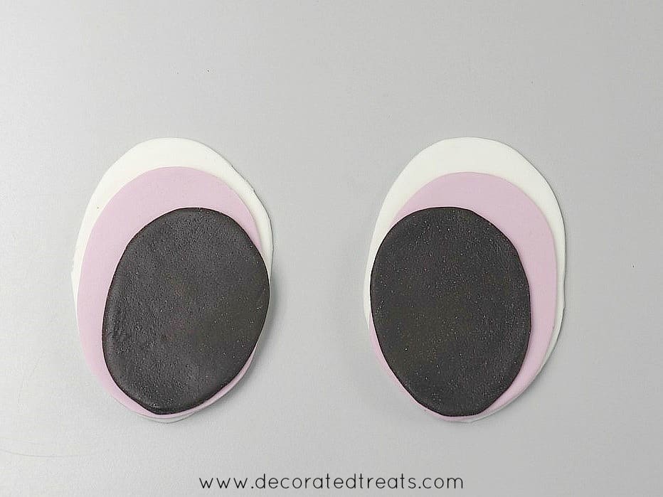 A set of 2 oval fondant cutouts in white, purple and dark brown stacked together