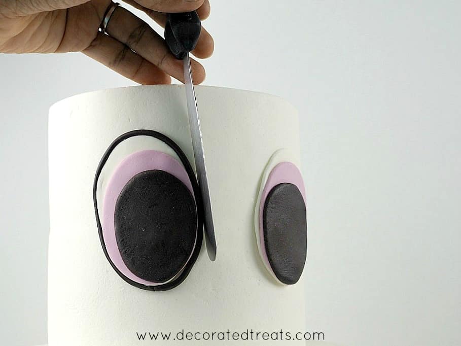 Using a palate knife to adjust the outline of the fondant eyes on the front of a two tier cake.