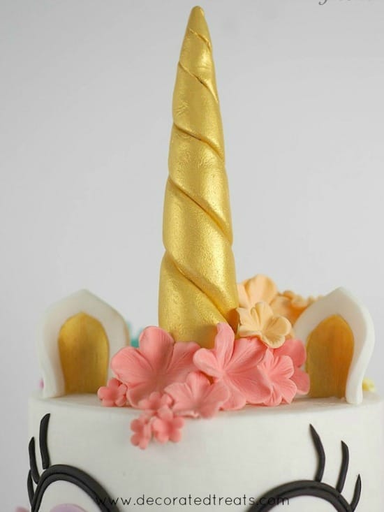 A two tier unicorn cake with eyes and golden horn