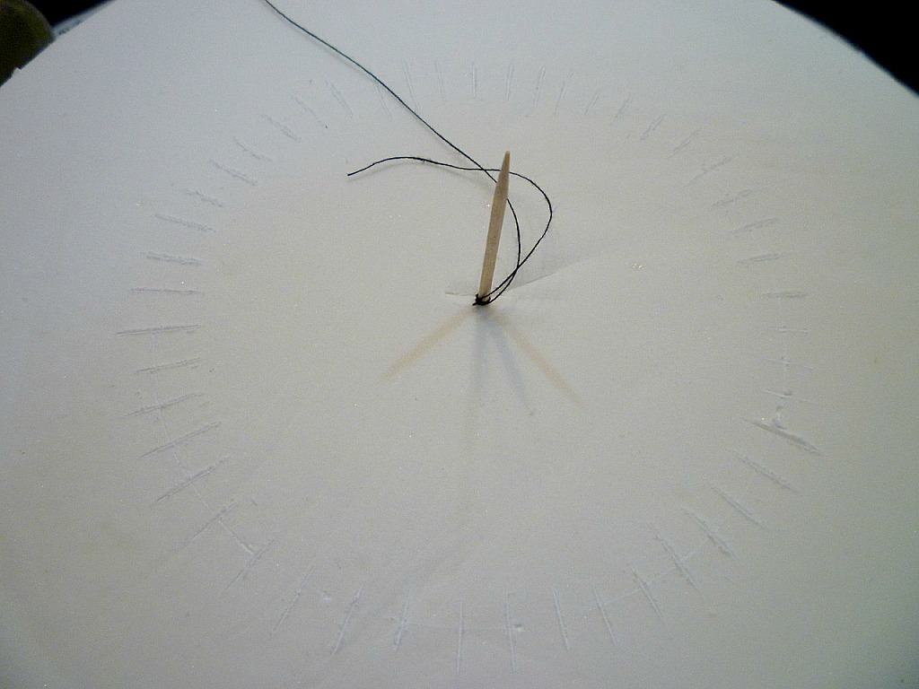 Thread poked in the center of a white fondant covered cake, with a thread tied to it