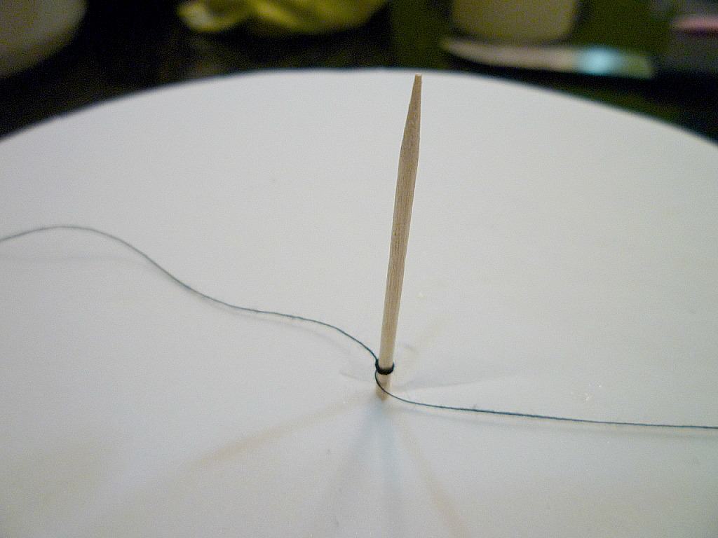 Thread poked in the center of a white fondant covered cake, with a thread tied to it