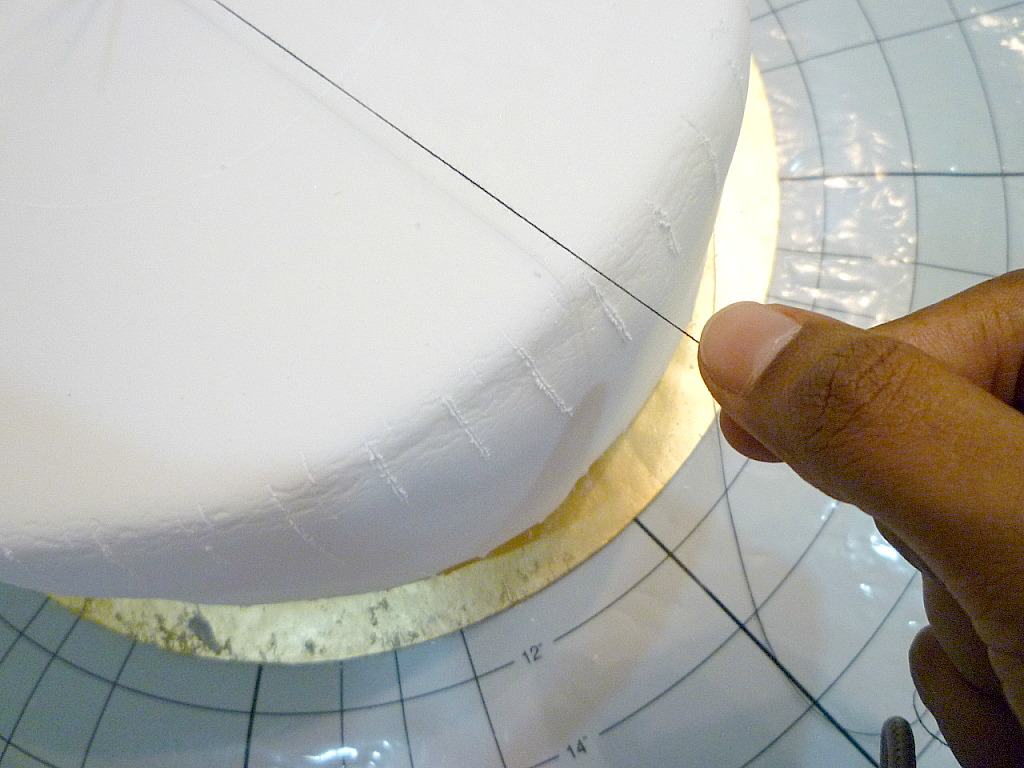 Pulling a black thread on a white fondant covered cake