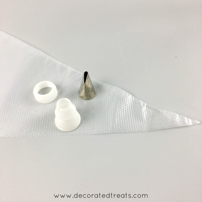 An icing tip, coupler and empty piping bag against a grey background