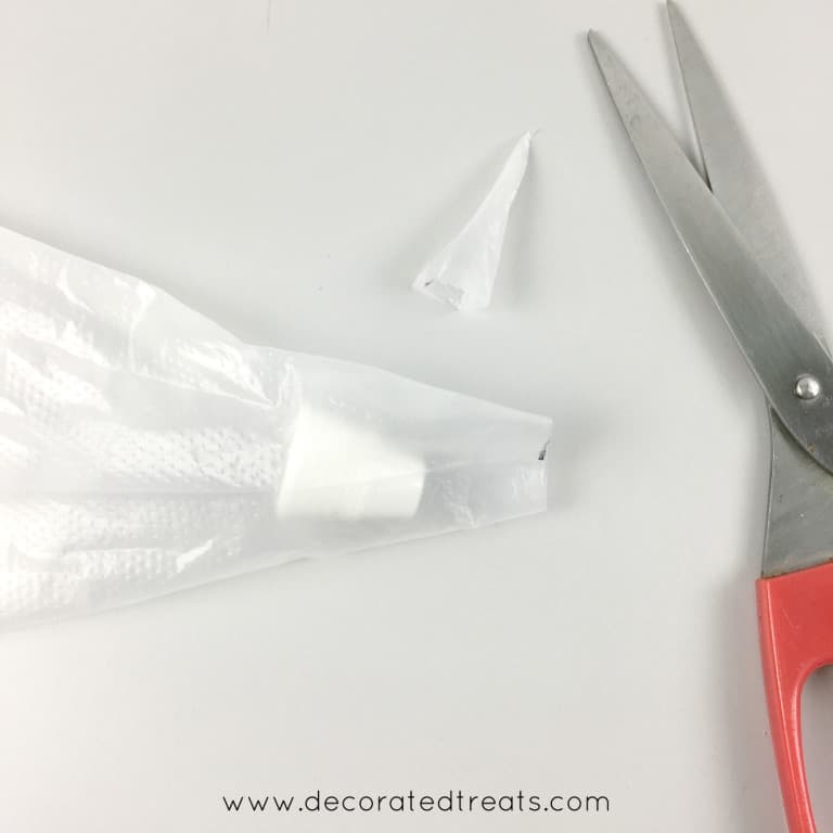A piping bag with a coupler in it and the tip cut off. In the background is a pair of red scissors