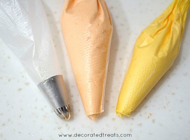 3 piping bag, one with a tip attached, 2 with orange and yellow icing without any tips