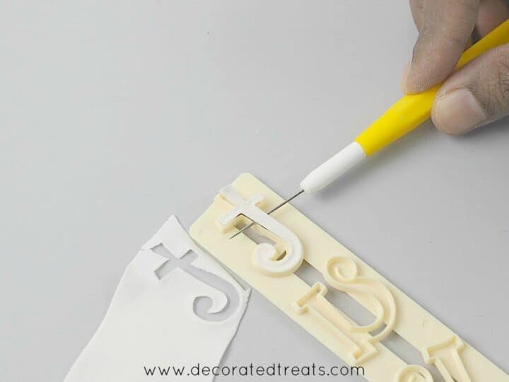 Using a needle tool to remove the gum paste from the alphabet cutter