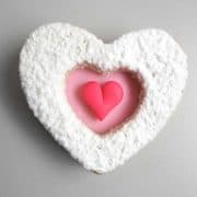 A heart shaped cookie decorated in pink heart and powdered sugar.