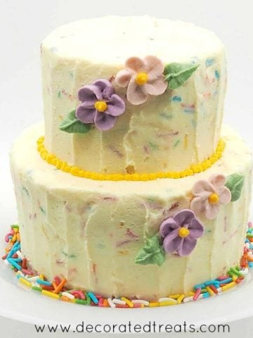 A 2 tier mini confetti cake in buttercream and pink and purple flowers