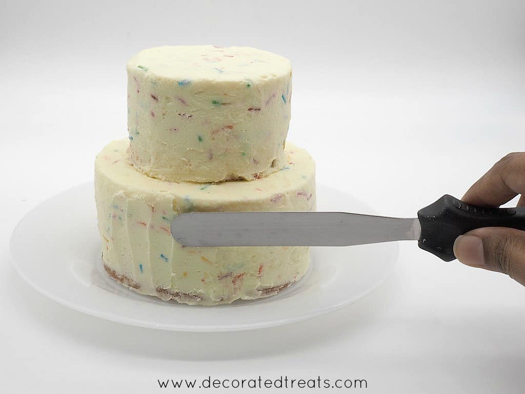 Using a palette knife to make lines on the sides of a 2 tier mini confetti cake