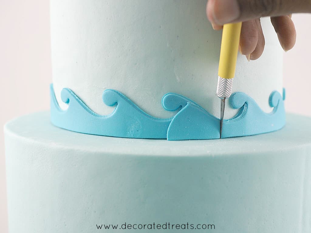 Using a sugar craft knife to cut off excess fondant waves border on a cake