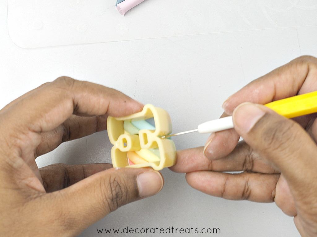 Using a needle tool to remove excess fondant of a fondant alphabet cutter.