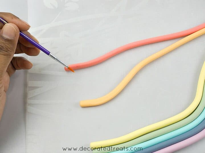 Applying glue with a brush to fondant strips in rainbow colors