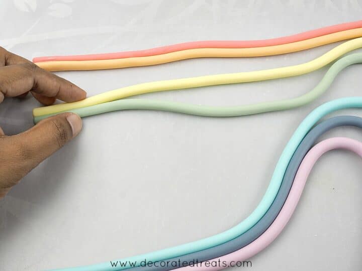 Pushing rainbow colored fondant strips together with hand