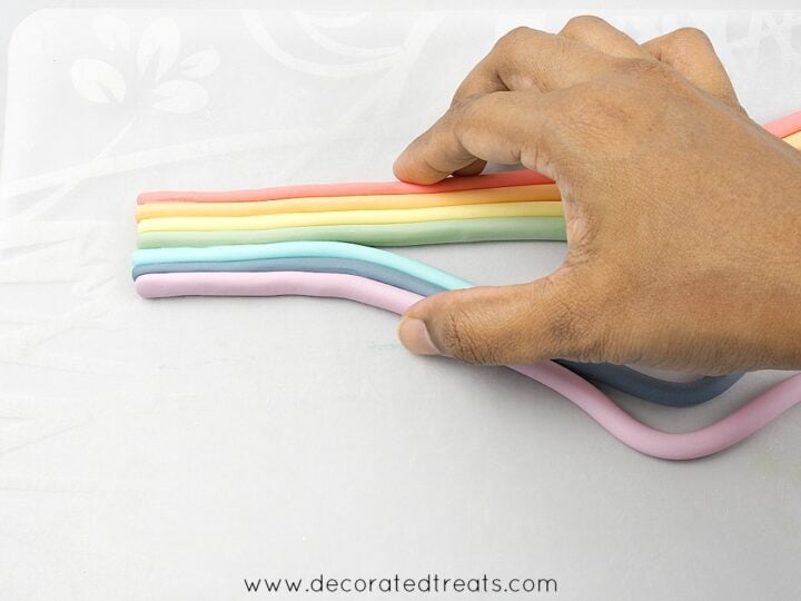 Pushing rainbow colored fondant strips together with hand