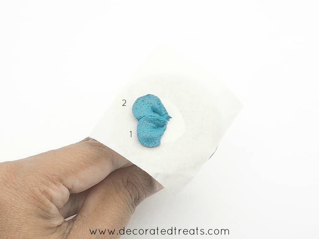 2 petals of a buttercream flower in blue piped on a parchment square held on a flower nail