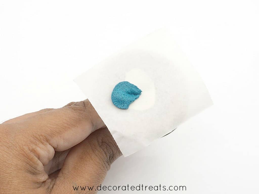 1 petal of a buttercream flower in blue piped on a parchment square held on a flower nail.