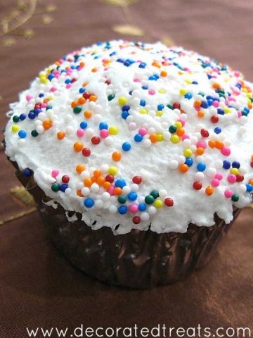 A cupcake in a silver casing, with white frosting and colorful sprinkles.