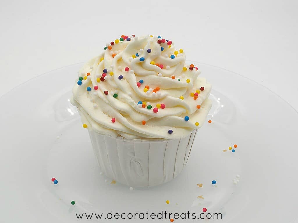A cupcake in white casing, with buttercream swirl topping and sprinkles