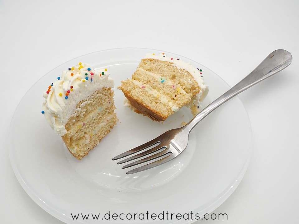 A layered cupcake, cut into half, on a white plate with fork