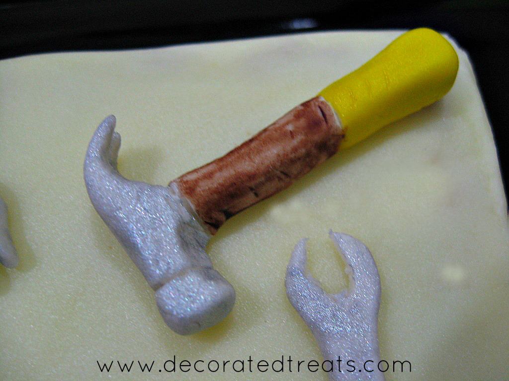Fondant hammer in yellow, brown and silver on a cake