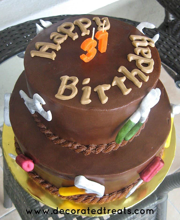 A 2 tier cake covered in chocolate frosting and decorated with fondant tools.