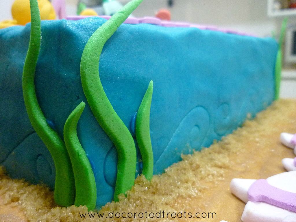 Sides of a buttercream covered cake decorated with fondant grass.
