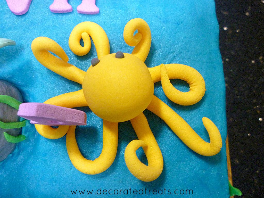 Top view of a yellow fondant octopus on a buttercream cake.