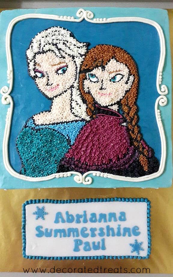 A square cake covered in blue icing with Anna and Elsa's images piped in buttercream