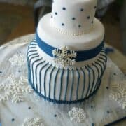 A three tier white cake decorated with blue stripes and white royal icing snowflake.