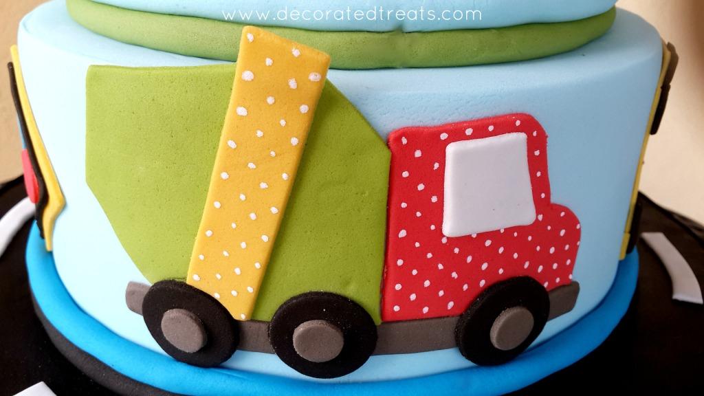 A green and red mixer truck cut out of fondant, on the sides of a cake
