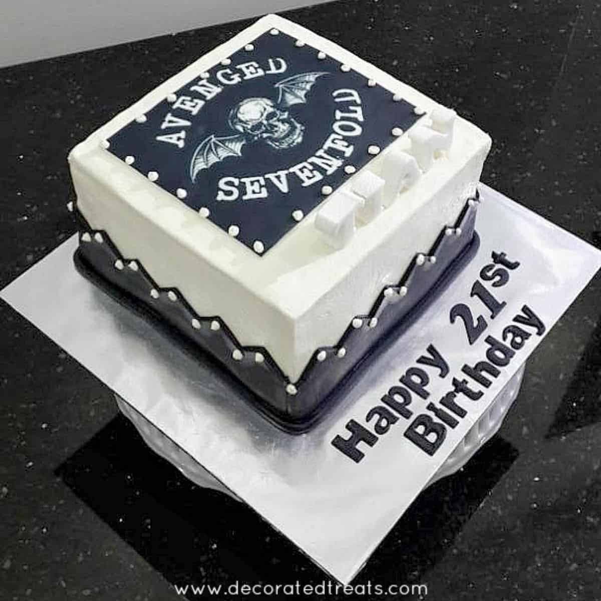 A square white cake decorated with Avenged Sevenfold image in black.