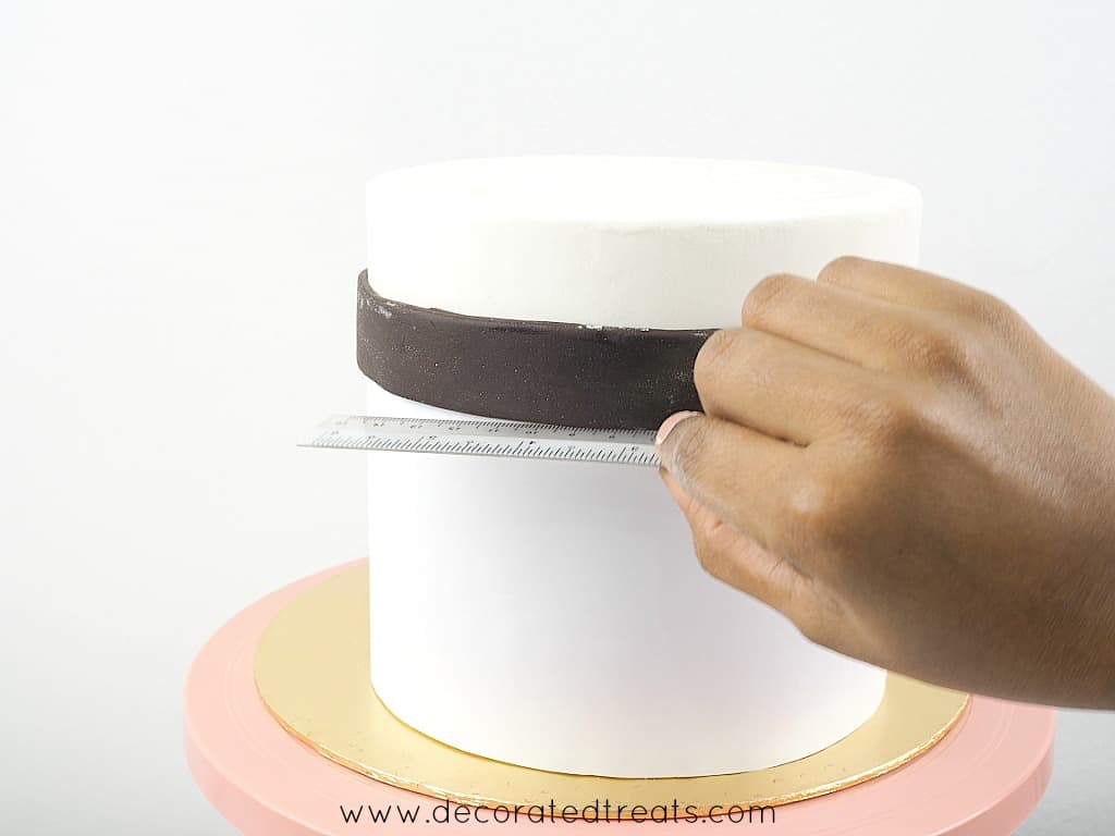 Using a ruler to adjust the height of a fondant strip around a cake
