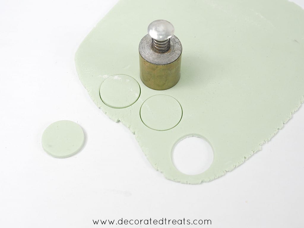Using a round plunger cutter to cut out green fondant for a baby shower cake.