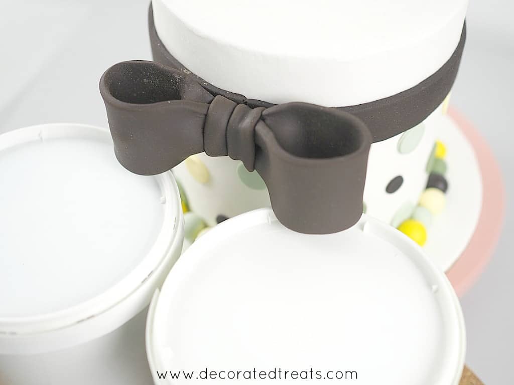 Supporting a brown fondant bow on the side of a baby shower cake with 2 fondant tubs