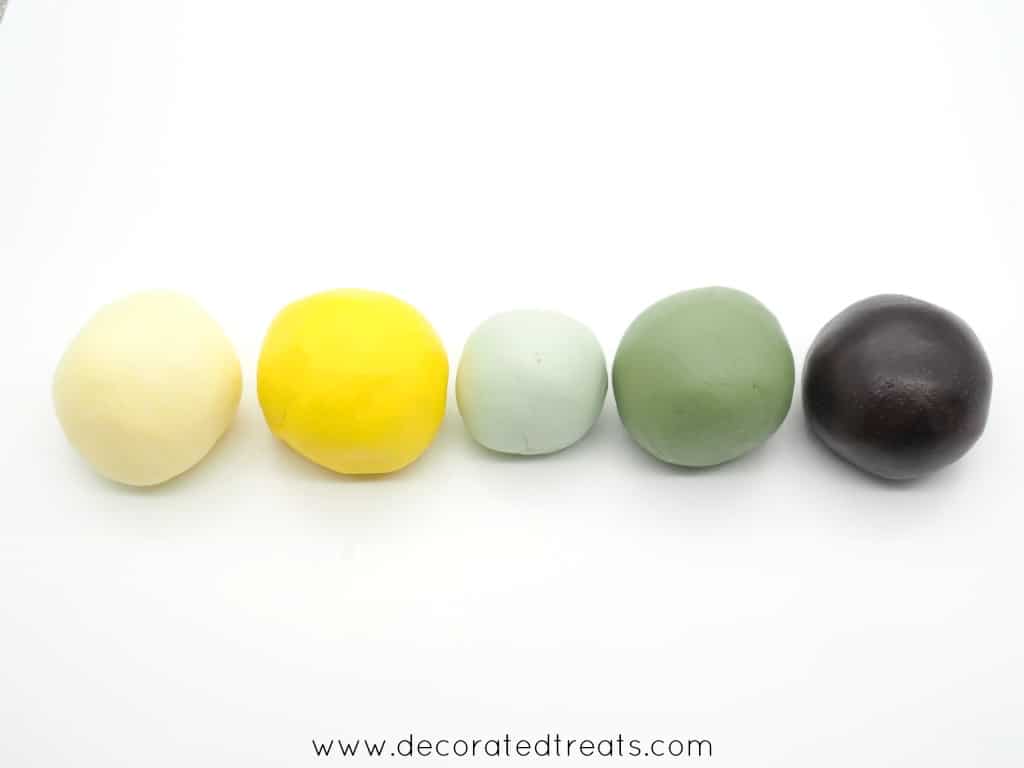 Fondant balls in light yellow, yellow, green, dark green and brown in a row for a baby shower cake.