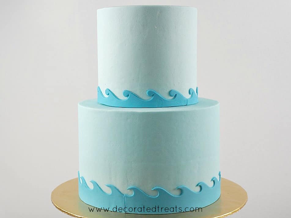 A 2 tier light blue cake with sea waves fondant borders