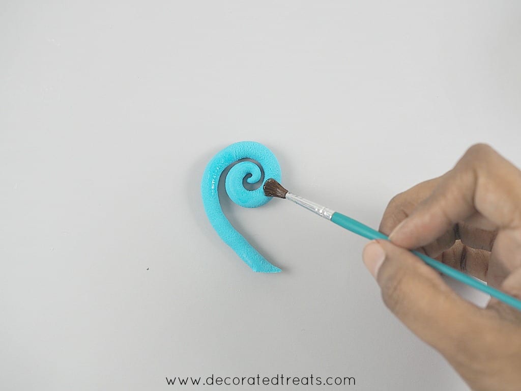 Using a small brush to brush a coiled blue fondant strip