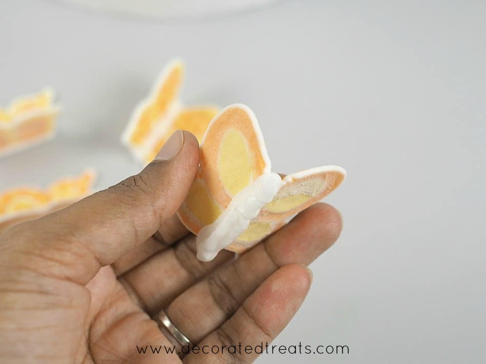 An orange royal icing butterfly held in hand