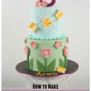 A 2 tier round cake in green and blue fondant. Bottom tier is decorated with fondant flowers and the top tier with royal icing butterflies in orange. Cake topper is a large glittery number 8