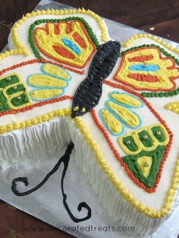 A butterfly shaped cake decorated in yellow, green, red and blue.