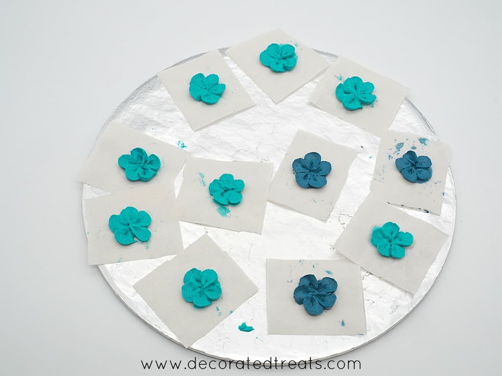 Turquoise and blue buttercream flowers on parchment squares on a cake board