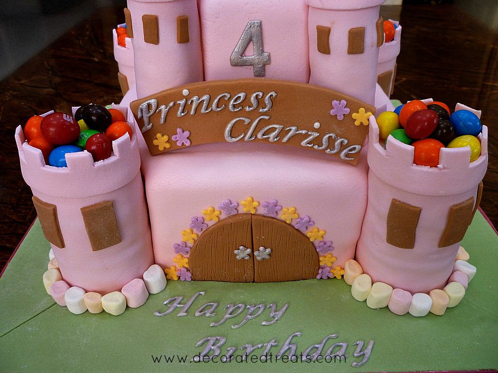 A 2 tiered castle cake in pink, decorated with mini marshmallows.