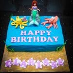 A Little Mermaid sheet cake decorated in buttercream and toy Ariel topper. On Ariel sides are fondant Sebastian and a yellow octopus.