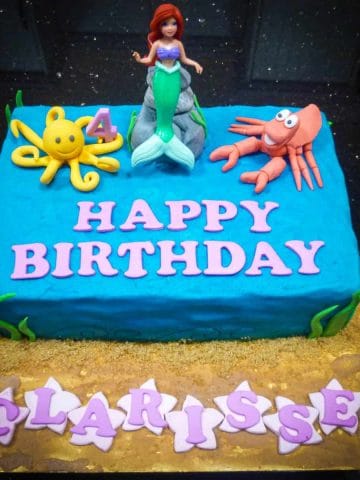 A Little Mermaid sheet cake decorated in buttercream and toy Ariel topper. On Ariel sides are fondant Sebastian and a yellow octopus.