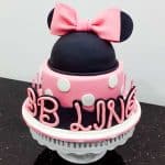 A round pink cake in white polka dots with a Minnie head in black decorated with pink bow.