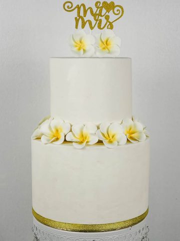 A 2 tier white cake with plumeria flowers and a Mr and Mrs gold topper.