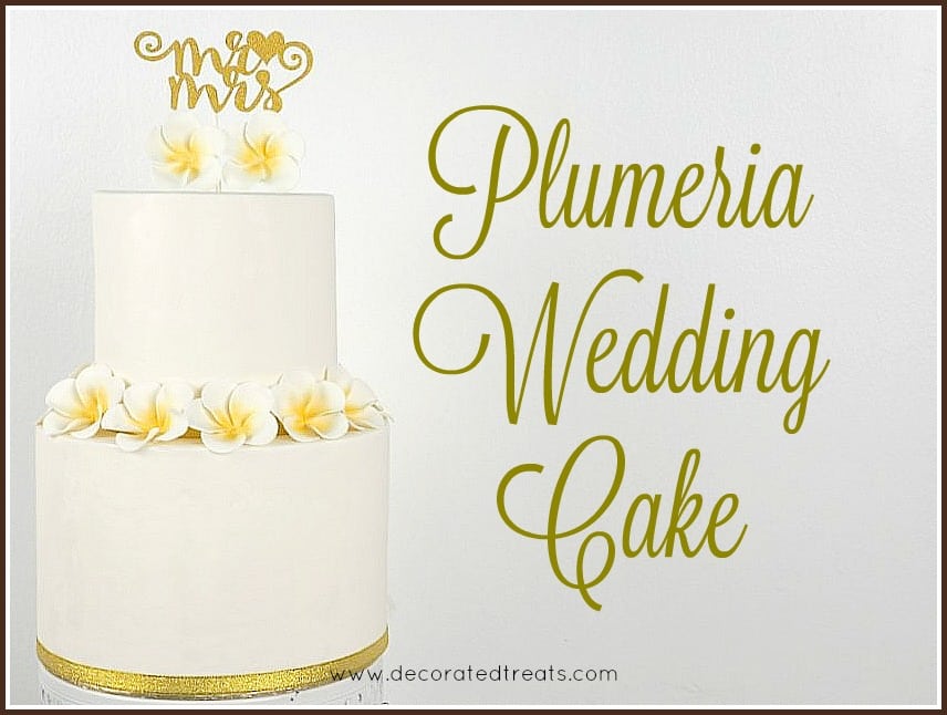 A 2 tier white cake with plumeria flowers and a Mr and Mrs gold topper